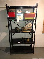 Front view of the black metal shelving unit with boxes and various household items on the shelves, showing size and condition.
