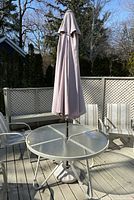 Outdoor round table with glass top and umbrella closed, displayed on deck with other outdoor furniture