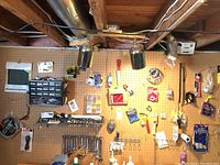 Wide view of pegboard with assorted tools, including wrenches, hand saw, screws, plastic drywall knife, electrical wires, and more mounted or hanging.