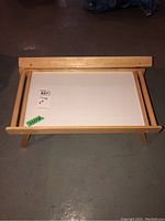 Top view of one wooden folding leg tray showing tray surface and folded legs underneath on basement floor.