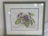 Frontal view of the framed watercolour painting of African violet flowers with green leaves in a pot.