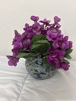 Purple artificial violets in a mottled blue and gray stoneware vase on a white background