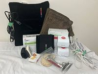 Lot showing black Thermos heat pad, brown heat pad, band-aid boxes, medical tools in small plastic case, and blood pressure cuff wires