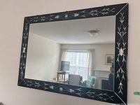 Full view of the rectangular mirror showing black frame with silver floral and linear designs reflecting room.