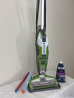 Full upright Bissell CrossWave Swivel multisurface floor cleaner with the two different brush rolls and a bottle of Bissell Multi-Surface Floor Cleaner placed beside it on a white sheet.