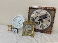 Five clocks visible: large white round wall clock, vintage world map clock in box, brass mantel clock with rotating pendulum, small white digital clock, small gold carriage clock