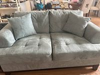 Front view of green loveseat with two cushions showing overall tufted upholstery and wide armrests.