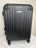 Front view of gray Canada hard-sided carry-on suitcase with ribs and Canada brand plaque, showing corner protectors and wheels