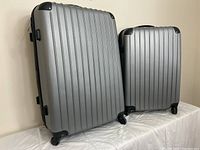 Two gray vertical ridged suitcases, one larger and one medium, standing upright showing front and side views, wheels visible.