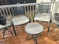 Full view of two green outdoor metal chairs with woven backs and cushions, round coffee table and two side tables on wood deck