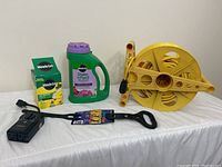 Full view of all included items in the lot on a white background showing the extension hose spool, Miracle-Gro Shake 'n Feed plant food, Miracle-Gro Ultra Bloom fertilizer bottle, extension cord strap, and Stanley outdoor timer.