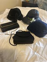 Three black hats and three black purses laid out on a bed showing styles and details