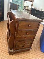 Front and side view of wooden side table showing five drawers with round wooden knobs and built-in magazine rack on the side.