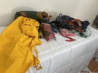 Wide view showing yellow raincoat, bundled leashes, boots, and cleats all arranged on white surface.