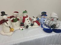 Six snowman holiday decorations arranged in a row on a white fabric background