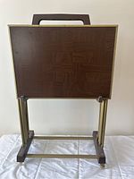 Front view of one TV table showing wood top with patterned wood design and brass coloured metal legs with caster wheels