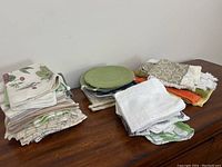 Overview of various kitchen linens folded and stacked on a wooden surface, including dish towels, drying towels, cloths, and hot plate liners.