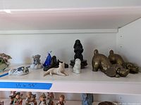 Shelf view showing a variety of small animal figurines including ceramic, wood, and glass cats and dogs with two brass dog door stops in front.