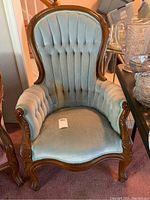 Front view of antique chair with light green velveteen upholstery showing stains and wear.