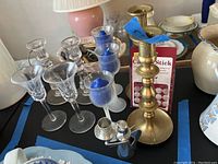 Photo showing seven clear glass candle holders with some having flared rims and varied shapes, three votive candles in glass holders, brass candlestick, and box of candle stickers.