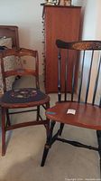 Two wooden chairs side by side, one with a floral cushioned seat and wooden back, the other a spindle-back wooden chair with floral top rail carving.
