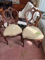 Pair of two hand-carved rosewood chairs with oval backrests and patterned upholstery on seats, placed side by side.