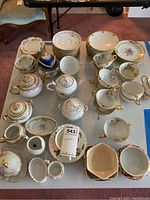 Wide view of multiple chinaware pieces including cups, saucers, teapots, cream and sugar sets arranged on table