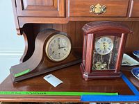Two clocks on wooden furniture: Seth Thomas mantle clock with rounded wood base and Bulova case clock with glass front and pendulum