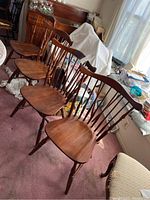 Four matching wooden dining chairs positioned in a room, showing their overall condition and style.