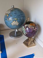 Photo showing two metal globes, one large blue ocean globe on a silver base, one smaller decorative purple/gold globe on a gold base.