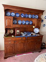Full view of vintage wild black cherry two-piece hutch with blue decorative plates on the upper shelf and clocks on the lower surface.