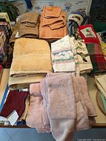 Overview of assorted bath towels, hand towels, and washcloths in beige, orange, yellow, and light pink colors stacked on a table.