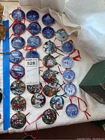 Wide view of 29 assorted Christmas ornaments including dated blue and white porcelain and colorful Disney character ornaments on white fabric surface