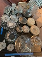 Overview of various cut glassware including bowls, plates, cream and sugar set, and vase, placed on a table with visible tufted chair in background