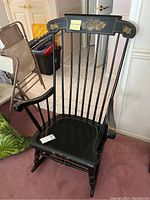Front angle view of black painted wooden rocking chair with floral designs on top back rail.