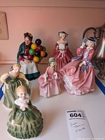 Six Royal Doulton porcelain figurines arranged on a counter, showing various angles and details