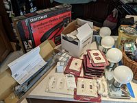 Overview of cordless scrubber box, vanity globe lights, light switch face plates, Windsor door closer, and Kohler plumbing parts on countertop.