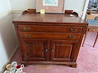 Front view of the wooden server cabinet showing two drawers over two cabinet doors with brass handles and round knobs.