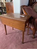 View of wood rectangular table with drop leaf sides folded down and visible wear on top surface
