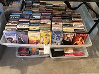 Photo showing a tub densely packed with VHS movies and TV shows, visible titles include 'Everything That Rises', 'Young Pioneers' Christmas', '007 License To Move', 'Basic Instinct', and others.
