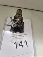 Photo showing a Chewbacca LEGO mini-figure with brown fur printing, bandolier detail, green eyes, holding a gray bowcaster weapon, positioned on a black display base against a white background.