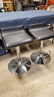 Pair of black counter height bar stools with curved seats and chrome bases shown side by side.