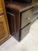 Angle view of the file cabinet showing two drawers with metal knobs, dark wood finish, showing some wear marks.