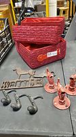 Two red woven baskets, cast iron welcome sign with horse, black cast iron hooks shaped like musical notes, and red cast iron spigots on table.