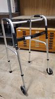 Side view of collapsible walker showing the aluminum frame, front wheels, padded hand grips, and adjustable legs.