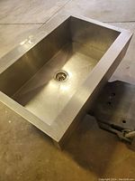 Top view of a large, rectangular deep stainless steel basin with a drain hole at the bottom center.