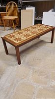 Full view of teakwood coffee table with mid-century modern design. Tabletop shows decorative tile inlay with floral motifs.