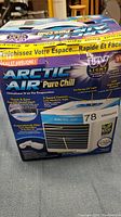 Front view of the Arctic Air Pure Chill evaporative air cooler in its original box with branding and key features visible.