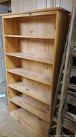Front view of unfinished solid pine bookcase showing five shelves and solid back panel in natural wood color.