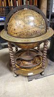 Front view of the globe drinks cabinet showing map print exterior, spiral legs, lower shelf